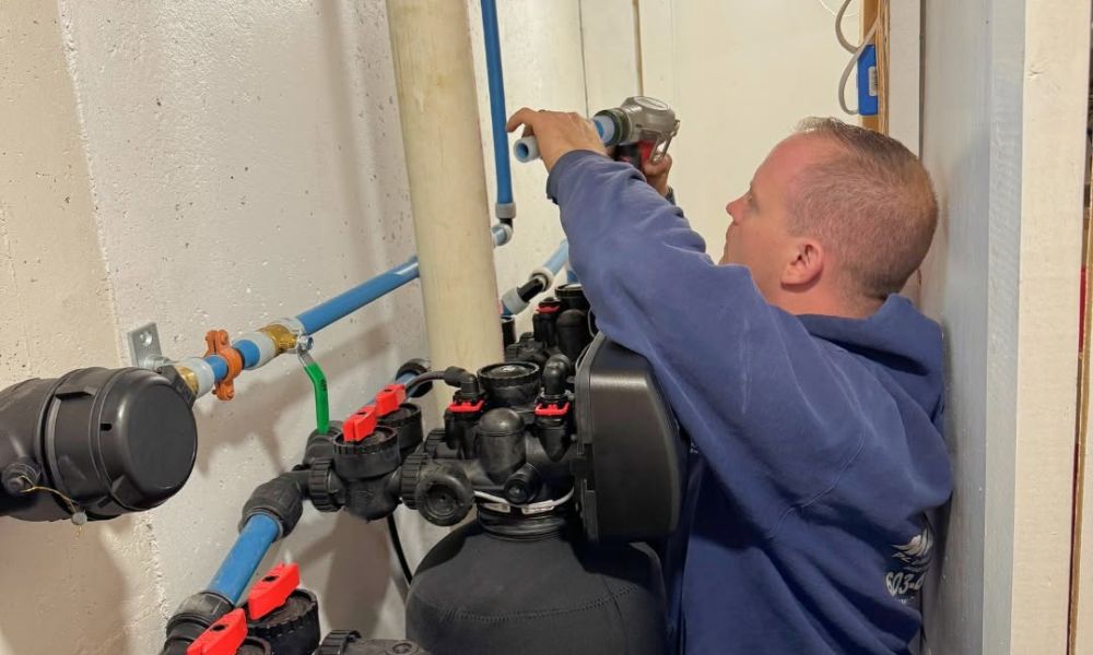 Technician installing home water filtration system in a basement, adjusting pipes for optimal function.