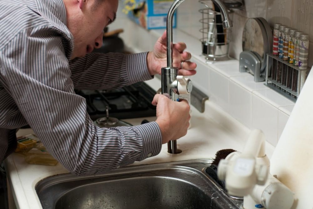 Person repairing kitchen faucet over sink, focused on plumbing maintenance.