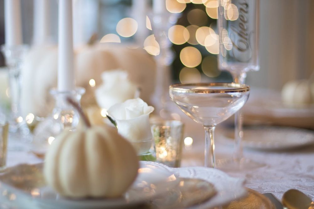 Elegant holiday table setting with gold-rimmed glasses, white roses, and mini pumpkins, creating a warm, festive atmosphere.