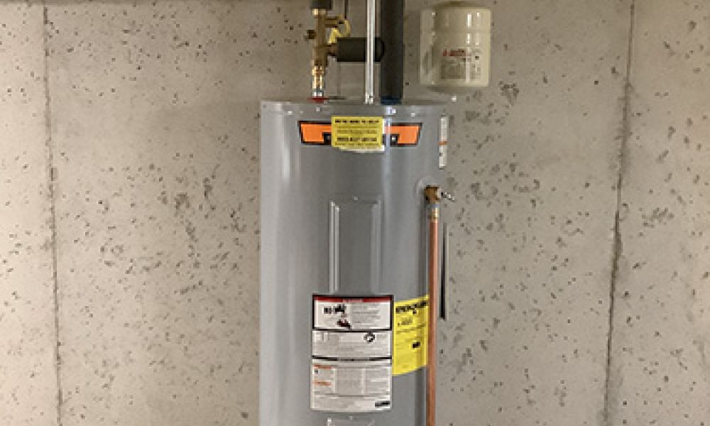 Basement water heater with pipes and insulation, installed against a concrete wall for efficient home heating.