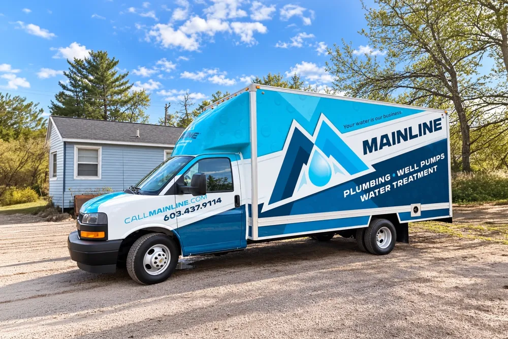 Blue Mainline plumbing truck parked near a house, offering well pumps and water treatment services.