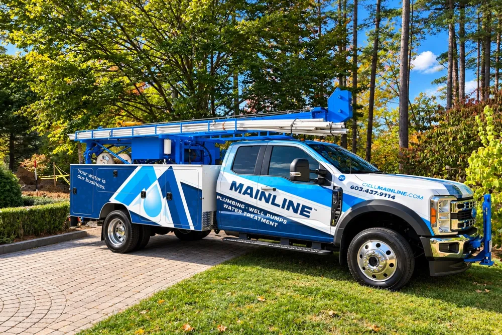 Mainline Plumbing truck parked on a driveway with trees in the background, showcasing water treatment services.