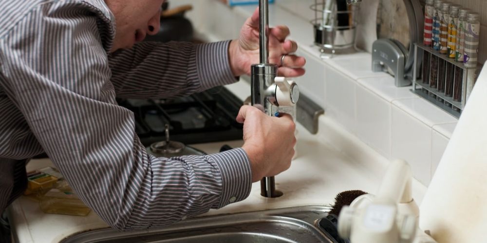 Person repairing kitchen faucet over sink, focused on plumbing maintenance.