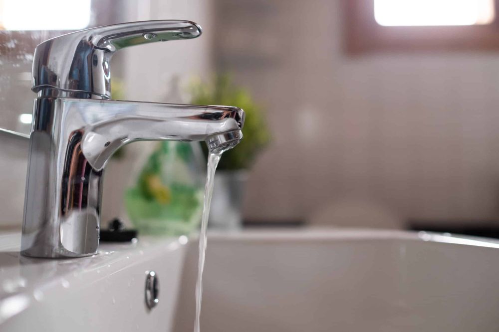 Water flows from modern silver bathroom faucet, highlighting sleek design and plumbing efficiency.