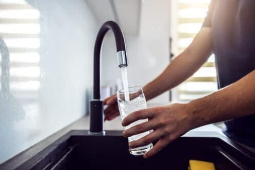 Person filling a glass with clean water from a modern kitchen faucet.