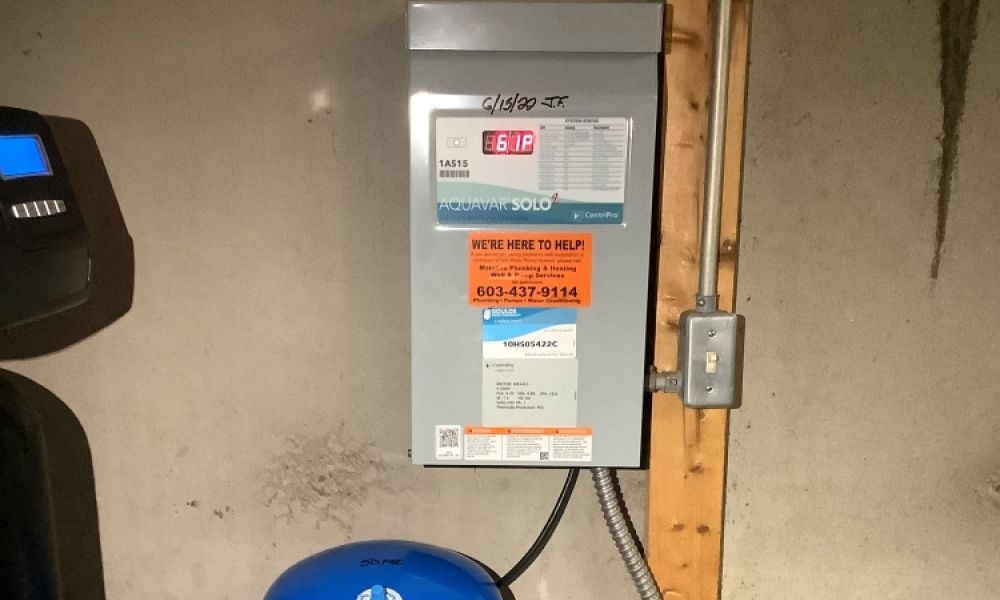 Water pressure system control panel with an orange service contact sticker in a basement setting.