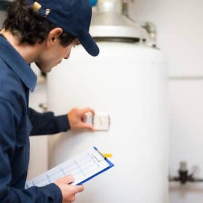 Technician inspecting water heater with clipboard in hand.