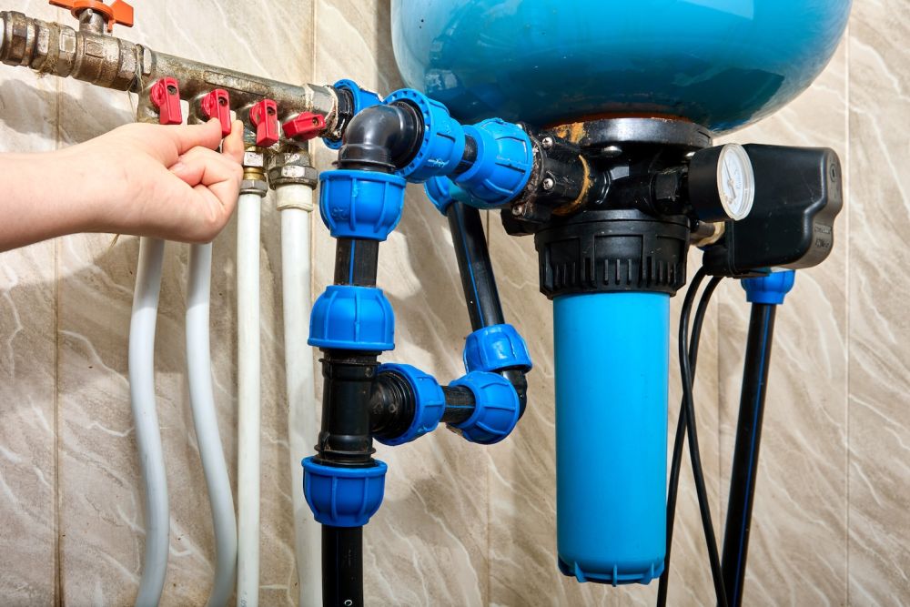 Person adjusting water filtration system valves, featuring blue and red components, ensuring efficient plumbing maintenance.
