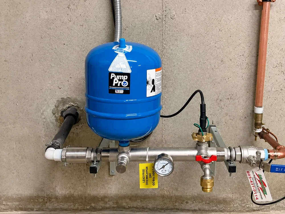 Blue water pressure tank with connected pipes and gauge against a concrete wall.