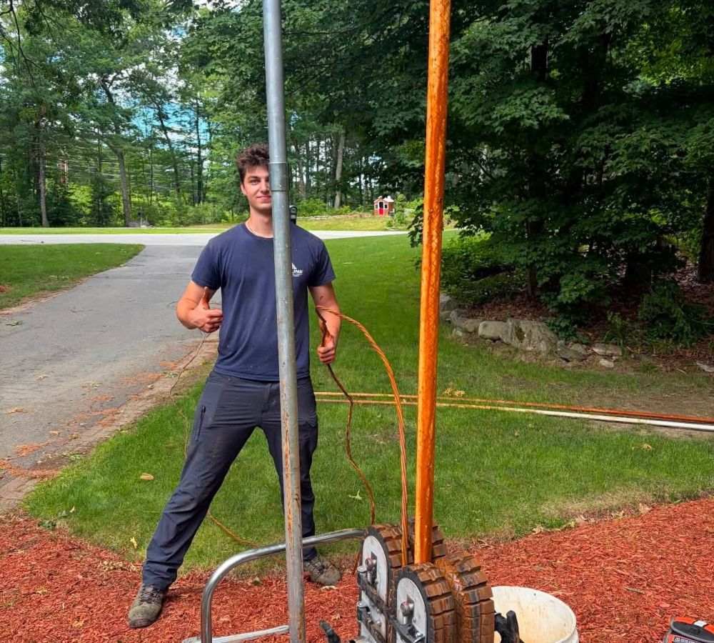 Worker operating a cable-pulling machine outdoors near a green area, on a sunny day.