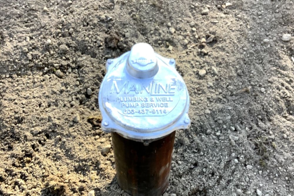 Metal well pump cover labeled Mainline Plumbing & Well on a dirt surface, providing water services information.