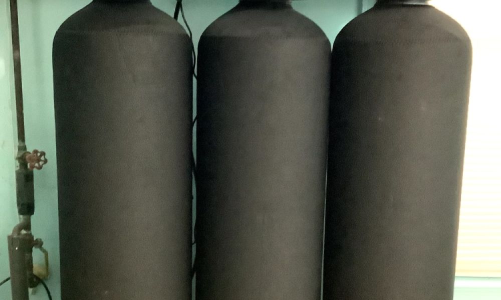 Three black water softener tanks with digital controls in a utility room setup.