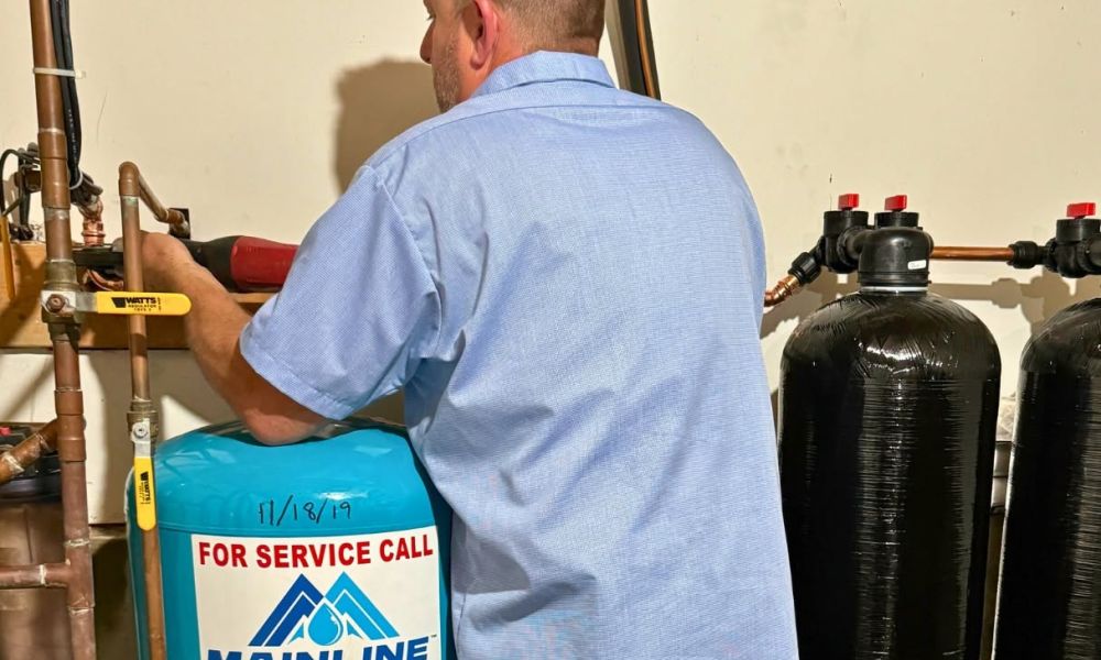 Plumber in uniform servicing water system with Mainline equipment in a utility room.