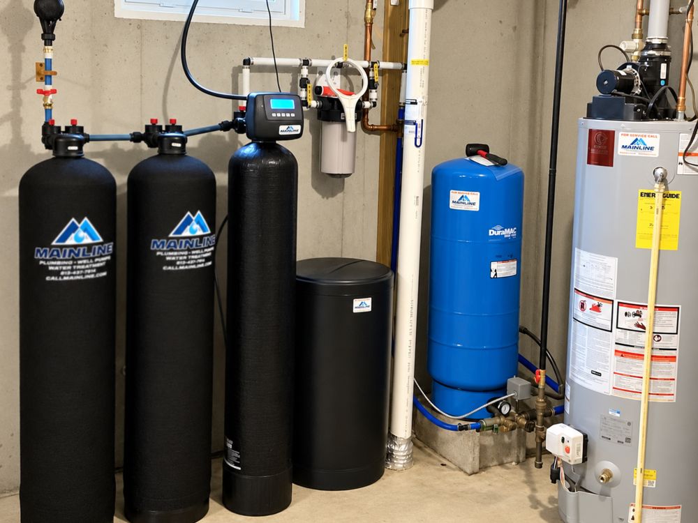 Basement water system with filters, water softener, and blue pressure tank next to a grey water heater on concrete floor.