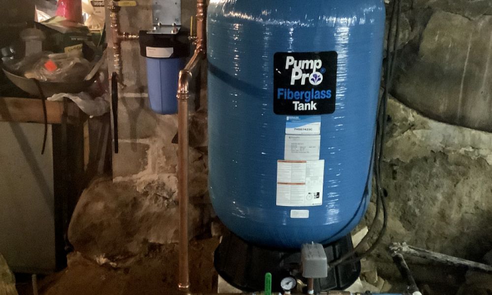 Blue Pump Pro fiberglass tank in basement. Surrounded by copper pipes. Used for water storage or filtration.