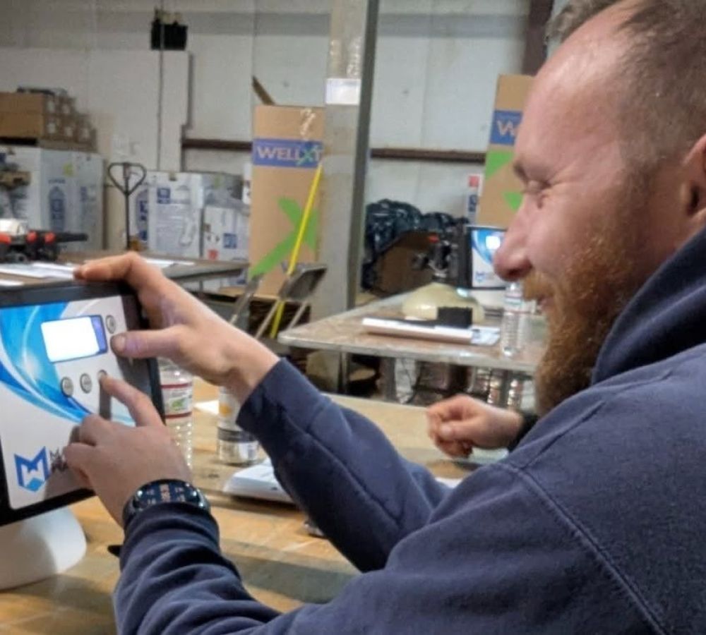 Man operating a digital control panel in a warehouse setting, smiling and engaged with the device.