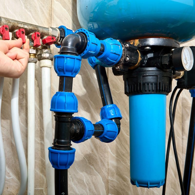 Person adjusting water filtration system valves, featuring blue and red components, ensuring efficient plumbing maintenance.