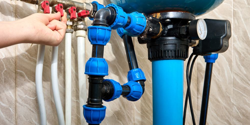 Person adjusting water filtration system valves, featuring blue and red components, ensuring efficient plumbing maintenance.