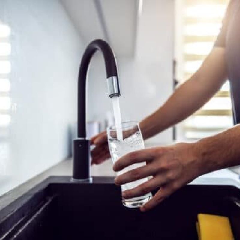 Person filling a glass with clean water from a modern kitchen faucet.