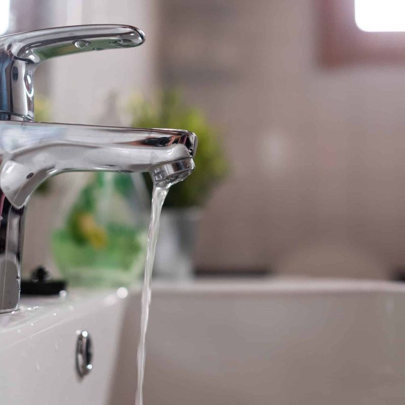 Water flows from modern silver bathroom faucet, highlighting sleek design and plumbing efficiency.